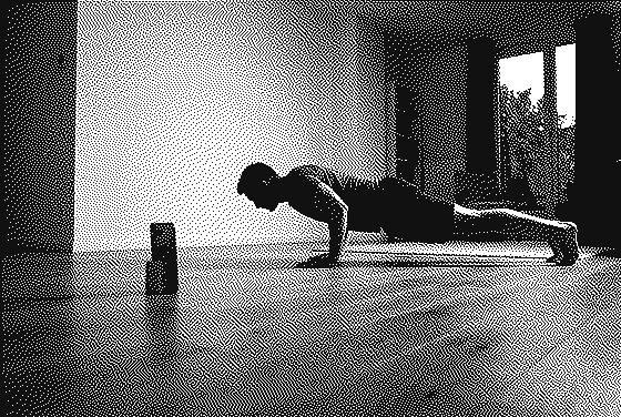 A person doing a push-up on a living-room floor, facing a phone standing upright on the floor.